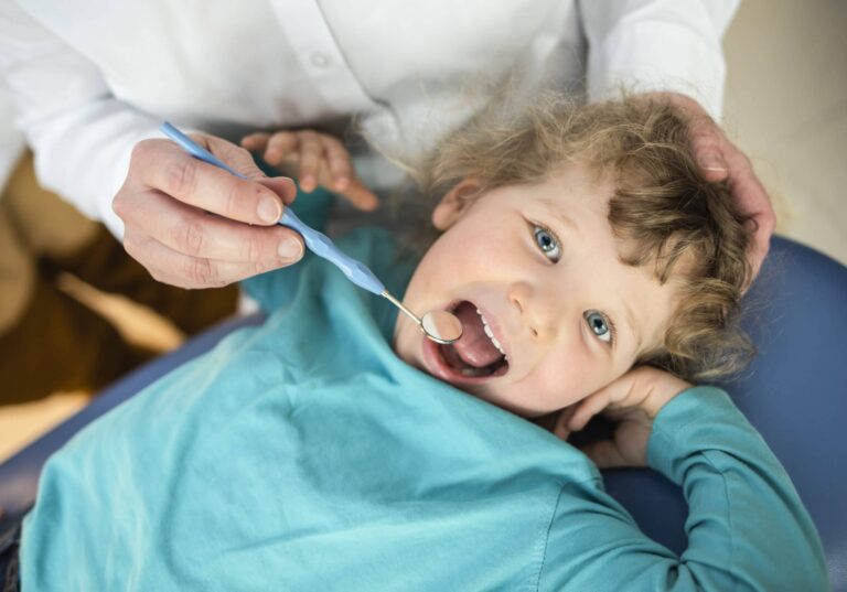 Kind liegt auf der Liege und Zahnärztin guckt in seinen Mund