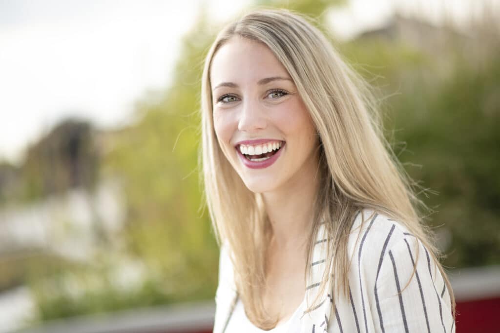 Eine Patientin hat neue Zähne mit sogenannten Veeneers ( hauchdünnen Verblendschalen) bekommen und strahlt mit der Sonne um die Wette.