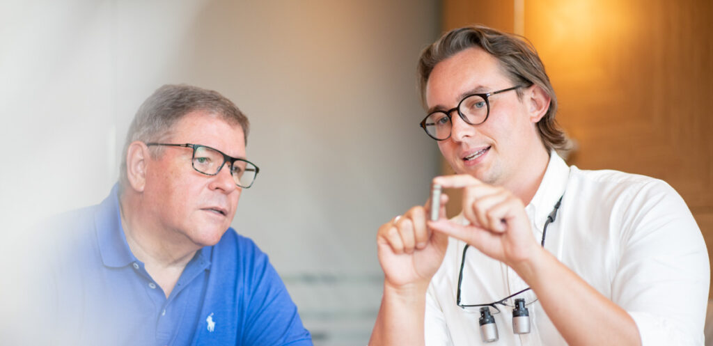 Dr. Schlotmann erklärt einem Patienten die Funktion eines Zahnimplantates und beide schauen auf das vergrößerte Implantatmodell.