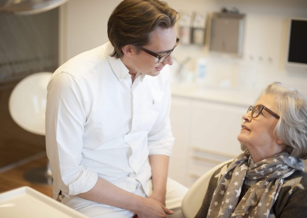 Dr. Schlotmann unterhält sich im Behandlungszimmer mit einer Patientin über die Behandlungsmethode der festen Zähne an einem Tag mit Sofortimplantaten.