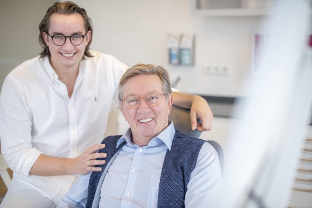 Älterer Mann mit Brille lächelt entspannt nach einer schmerzfreien Zahnbehandlung.